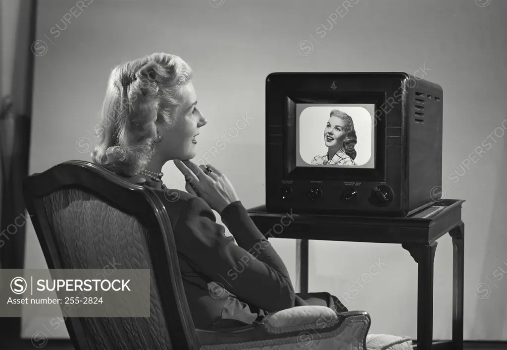 Vintage Photograph. Back view of woman sitting in front of television with smiling woman's face on screen