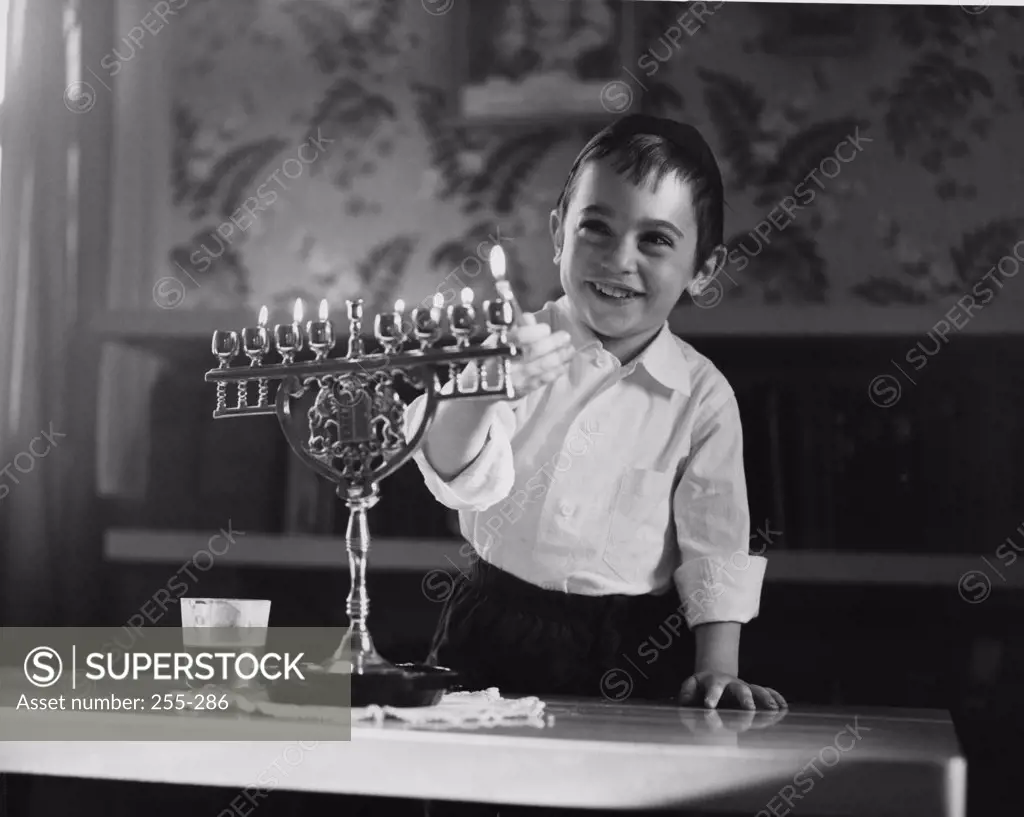 Boy lighting menorah candles and smiling