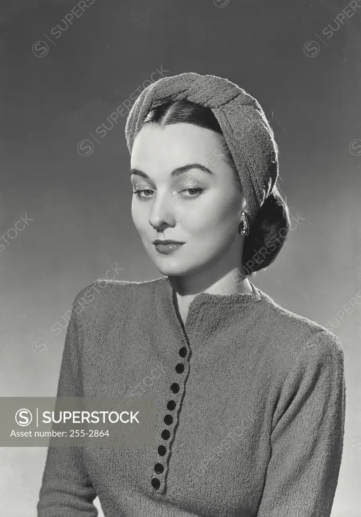 Brunette woman wearing knit blouse with black buttons and knit head wrap looking down