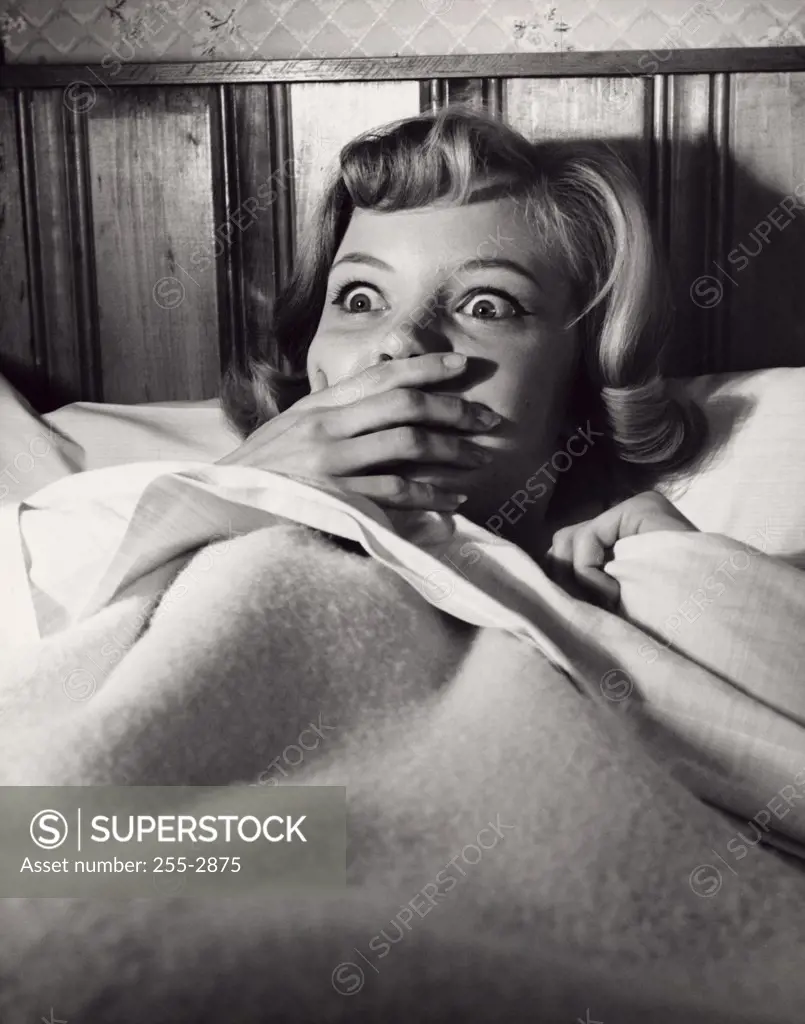 Close-up of a young woman lying in bed looking frightened