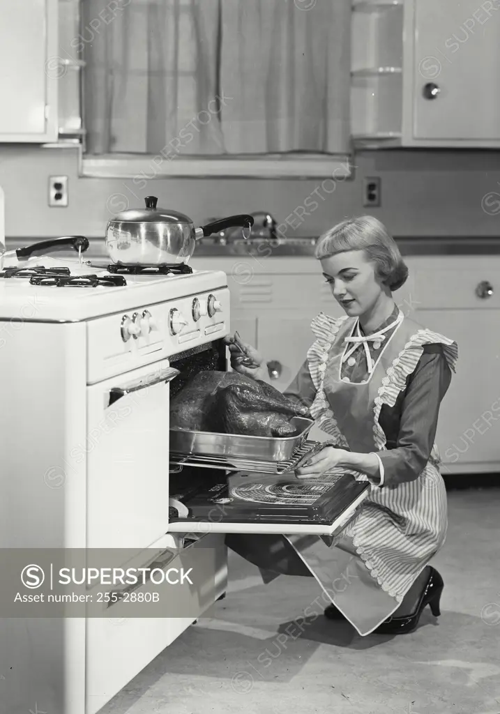Vintage Photograph. Woman in apron basting turkey in oven. Frame 1