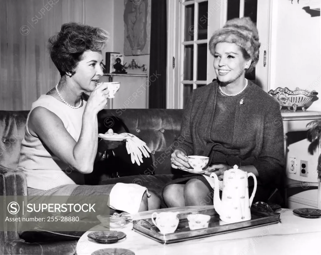 Two women drinking tea and talking in living room