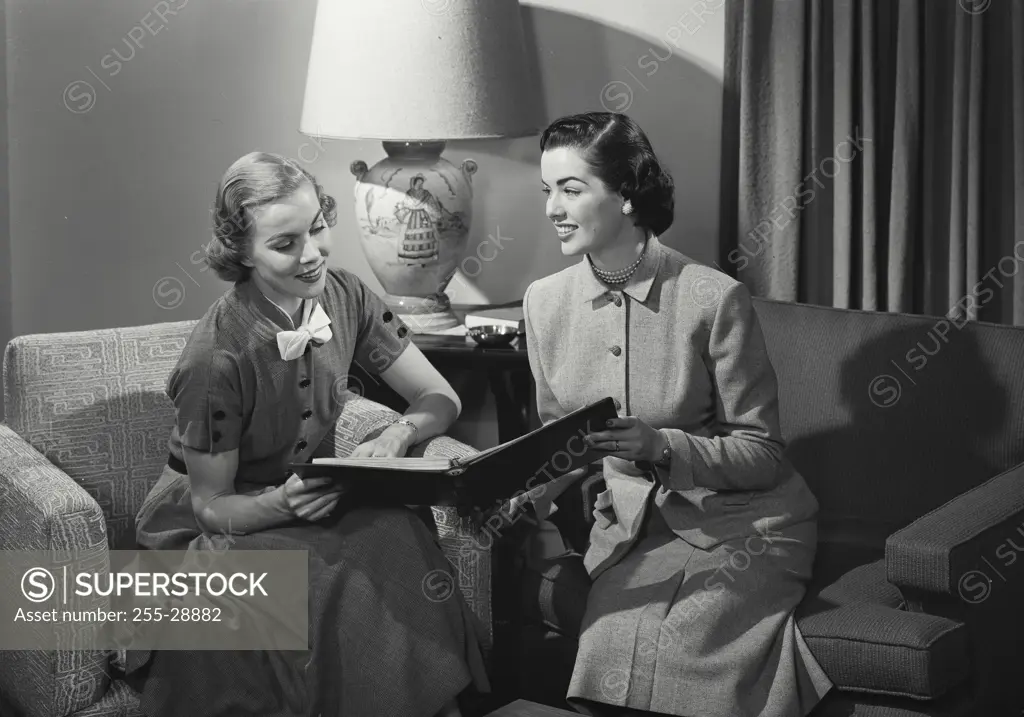 Vintage Photograph. Two smiling women sitting in living room looking at photo album together