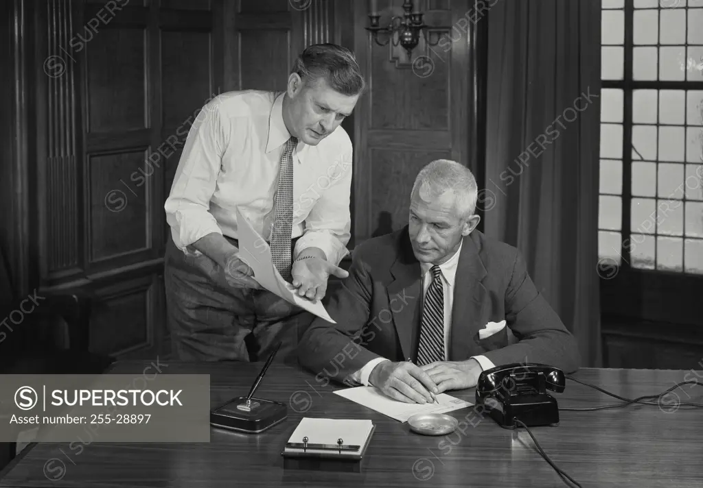 Vintage Photograph. Two business men in office discussing document. Frame 2