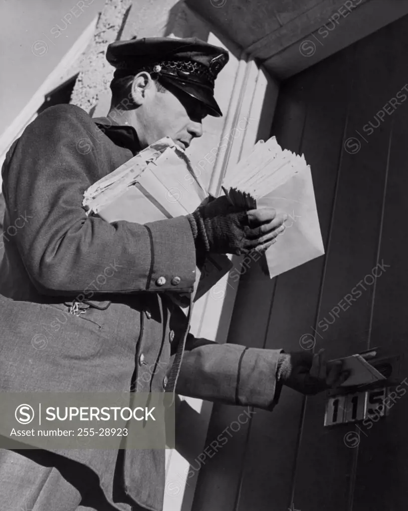 Postman dropping mail in mail slot, low angle view