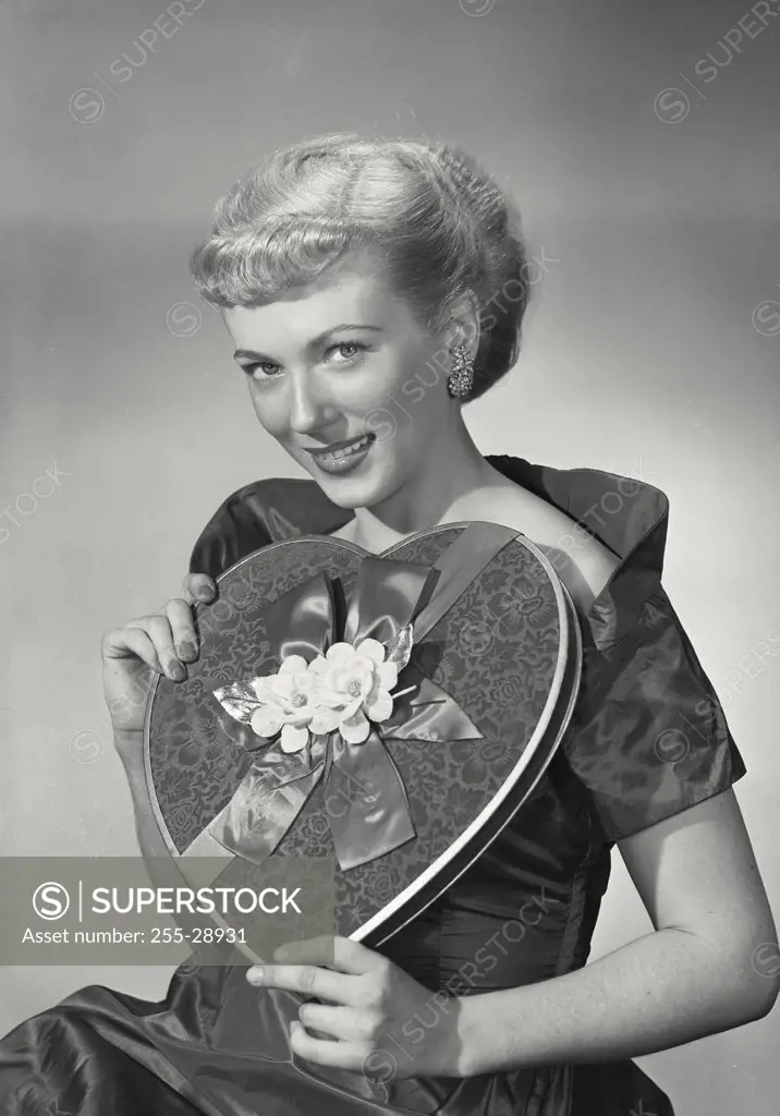 Vintage photograph. Woman in elegant dress smiling and holding heart-shaped box of chocolates