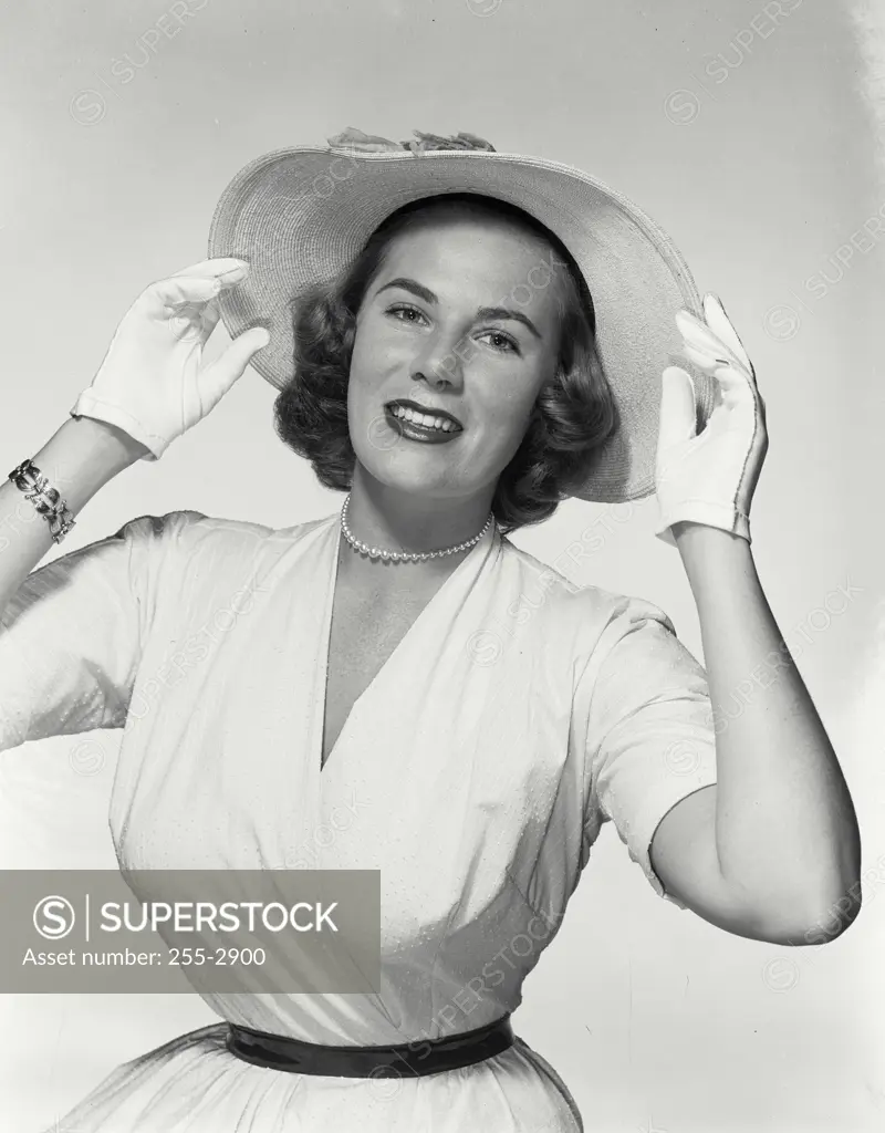 Vintage Photograph. Young woman smiling wearing large summer brim hat with both hands holding hat