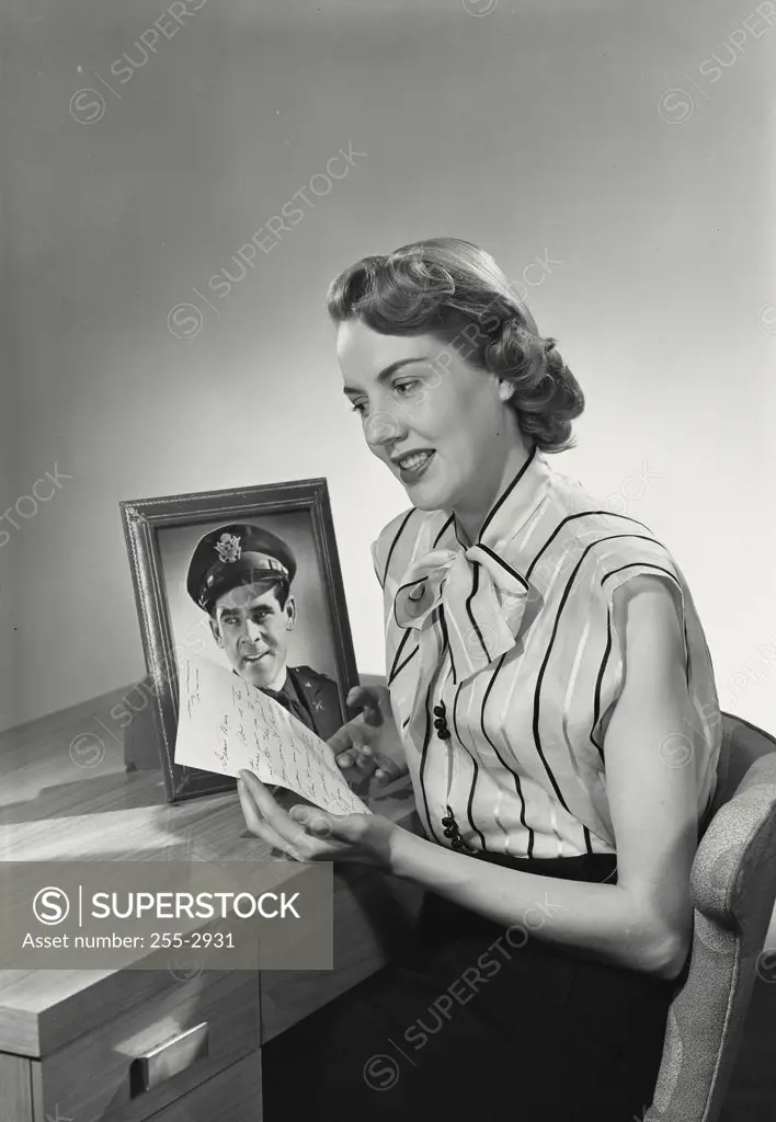 Vintage photograph. Woman sitting at desk with letter and framed picture of military officer husband