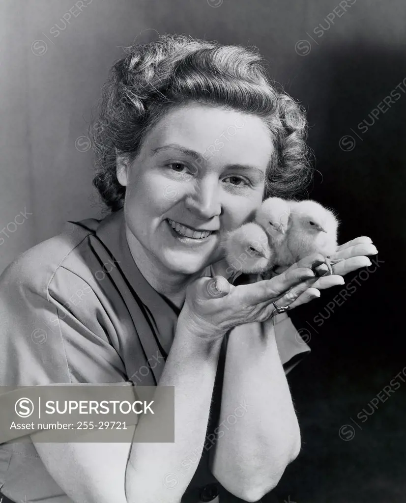 Portrait of a young woman holding three baby chicks in her palm