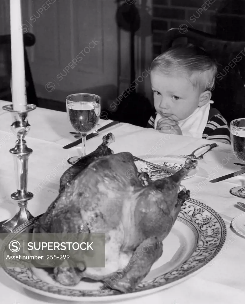 High angle view of a boy sitting at a dining table and looking at a roasted turkey on Thanksgiving day