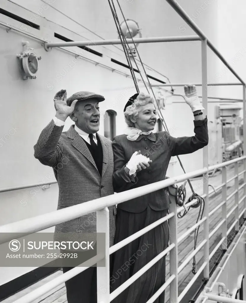 Senior couple standing on the deck of a cruise ship and waving