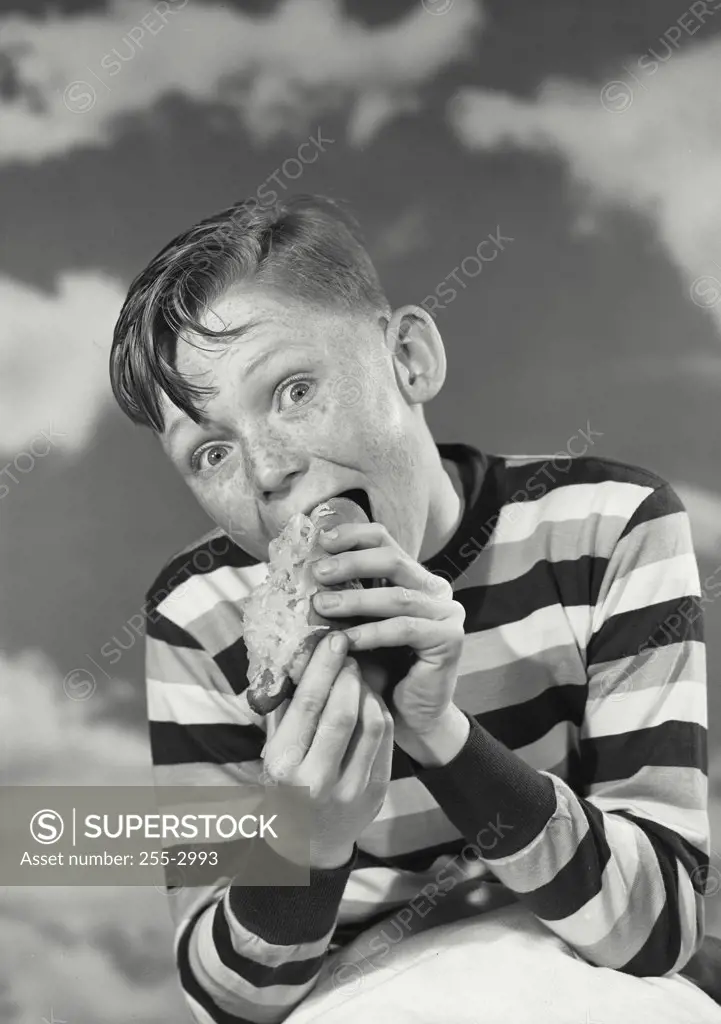 Vintage photograph. Young boy with funny expression eating hot dog.