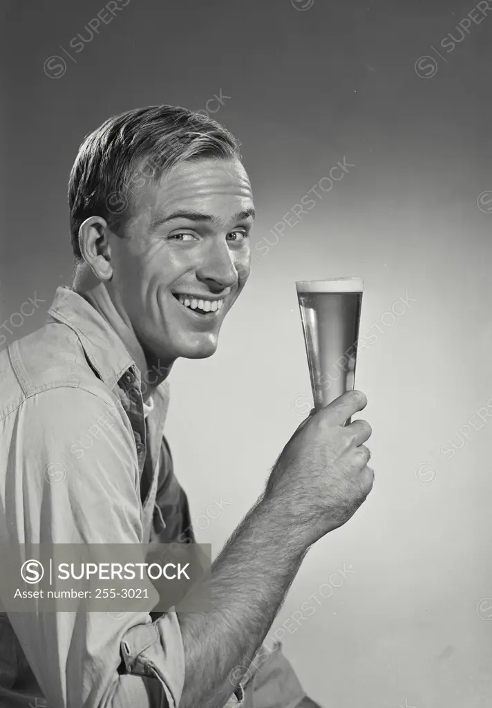 Vintage Photograph. Man wearing work shirt holding up glass of beer smiling