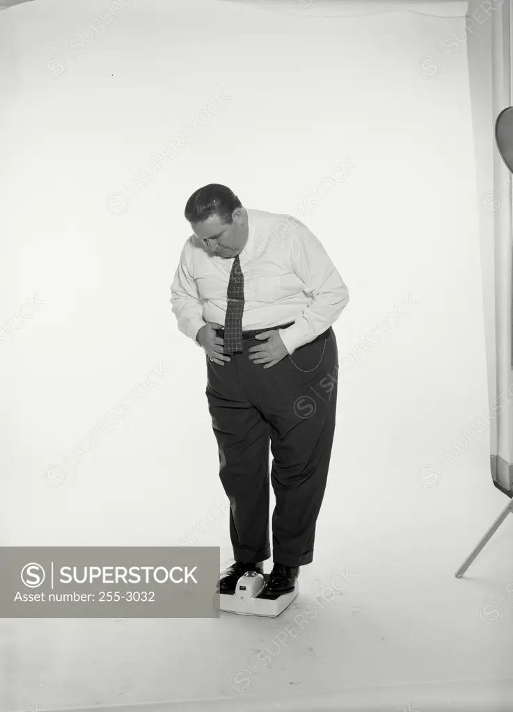 Vintage Photograph. Fat man standing on scale wearing dress shirt and tie holding stomach, Frame 2