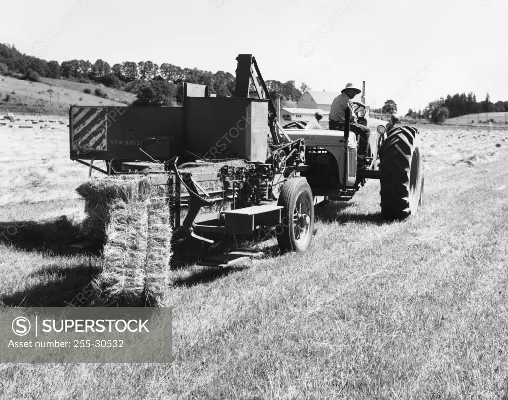 Farmer sitting on a tractor pulling hay baler in a field