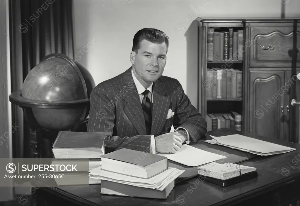 Man in suit behind desk surrounded by books