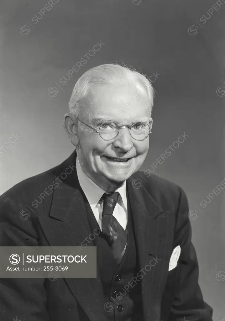 Elderly man with white hair wearing glasses and suit and tie smiling