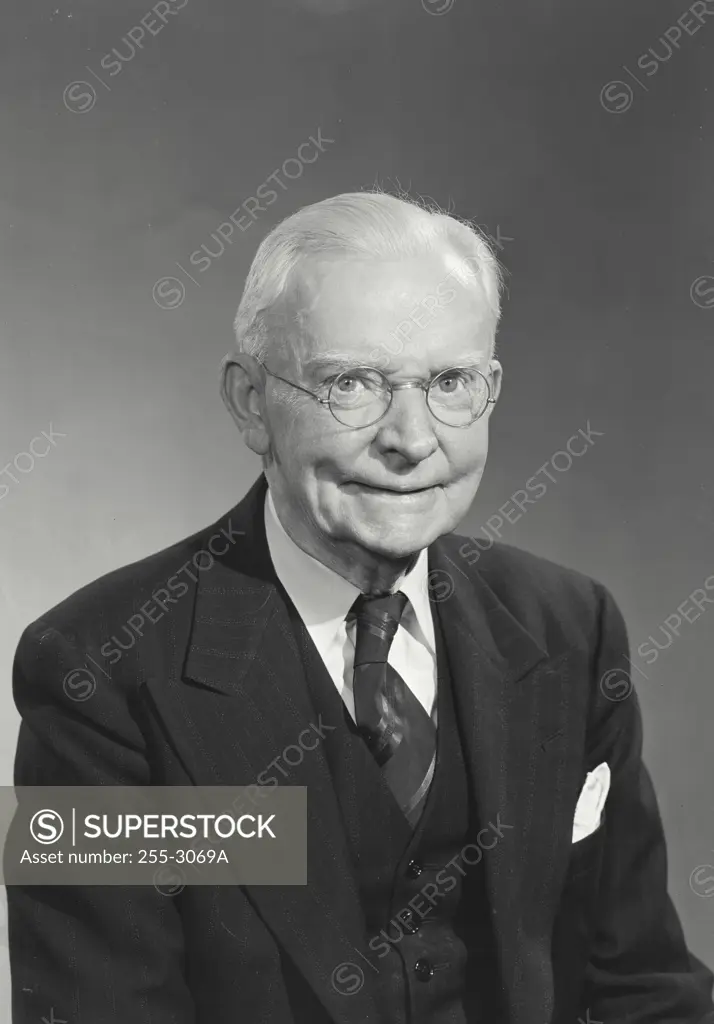 Elderly man with glasses and white hair wearing suit and tie smiling