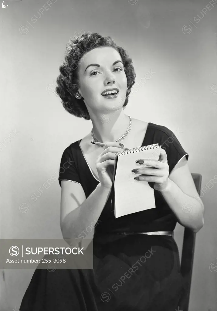 Vintage photograph. Portrait of young woman smiling writing on notepad.