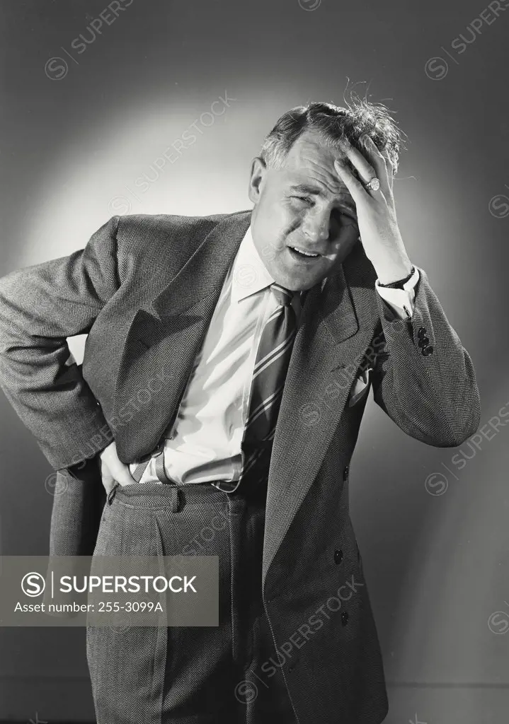 Vintage photograph. Man in suit and tie holding back with hand on forehead in pain