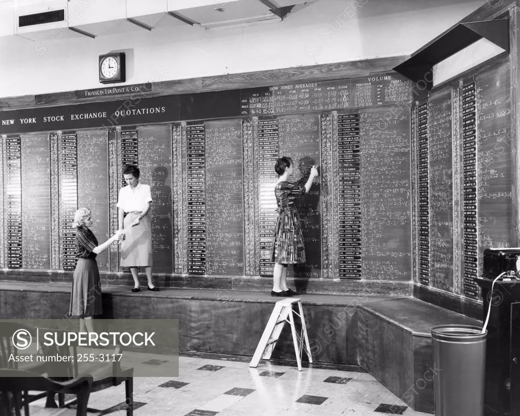 Three women writing on a blackboard at a stock exchange
