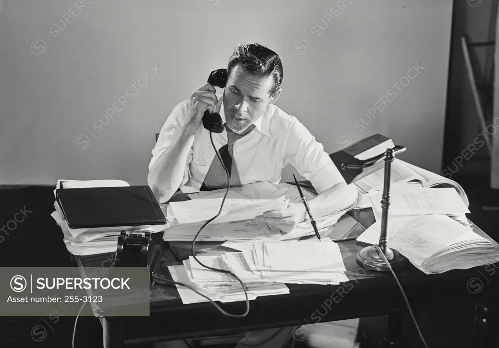 Vintage photograph. Man on telephone looking upset at desk filled with documents