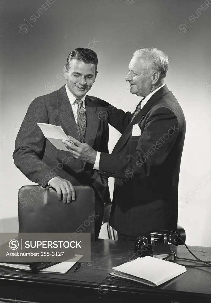 Vintage photograph. Young man and older man standing behind desk together looking at paper