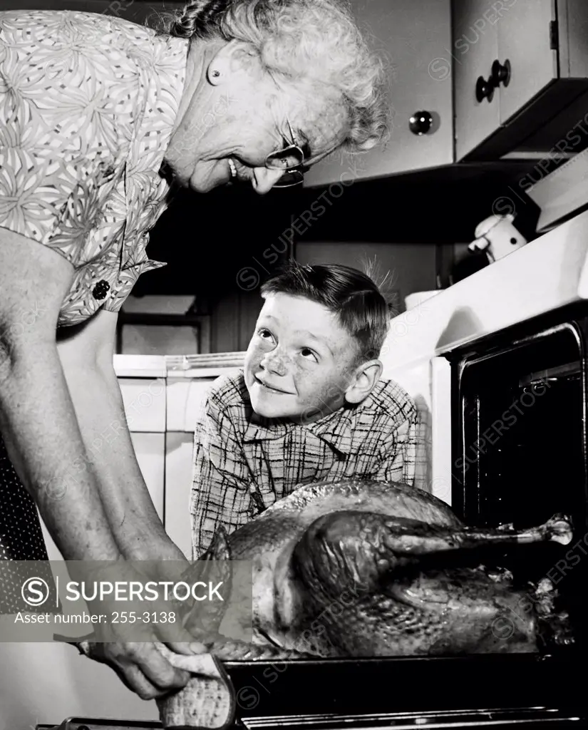 Grandmother taking a turkey from the oven with her grandson watching