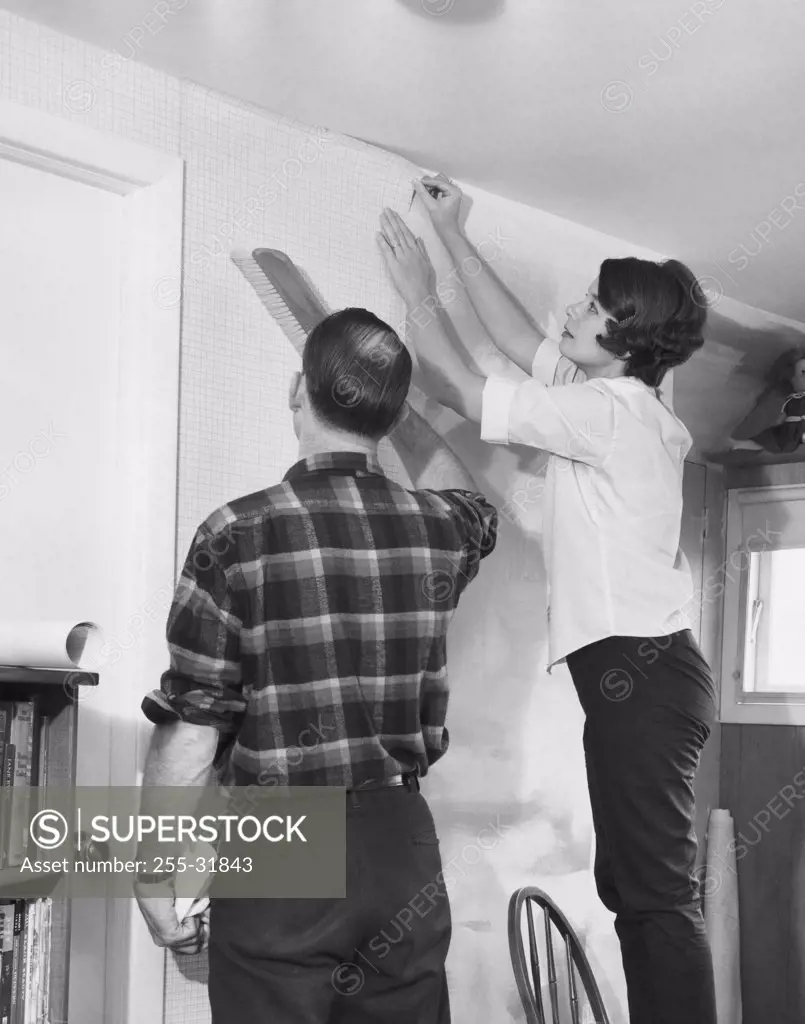 Mid adult couple applying wallpaper in a room