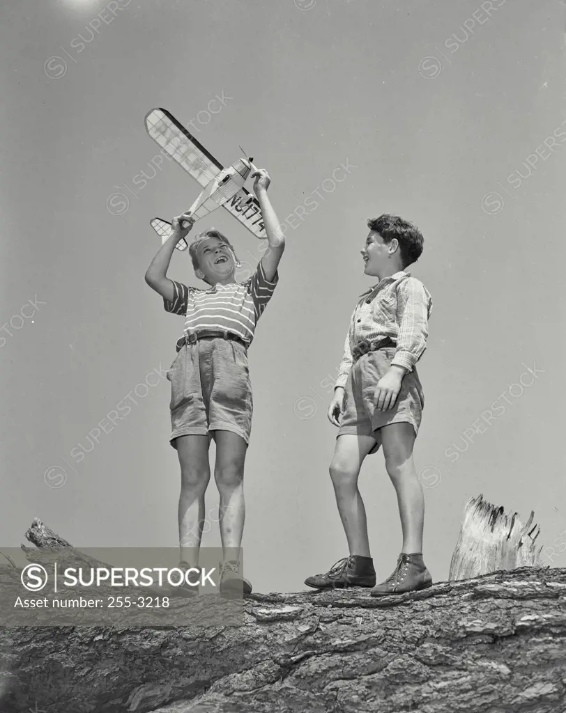 Vintage Photograph. Low angle view of two boys playing with a model airplane