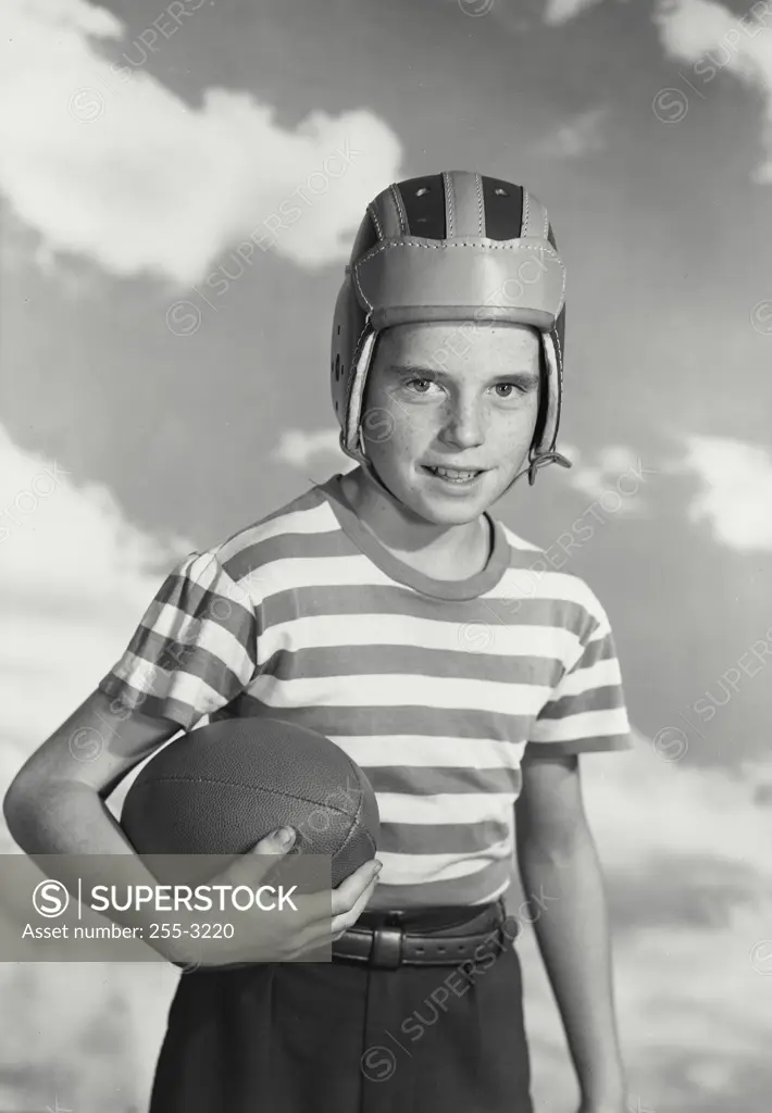 Vintage photograph. Boy in striped shirt and vintage football helmet smiling while holding football