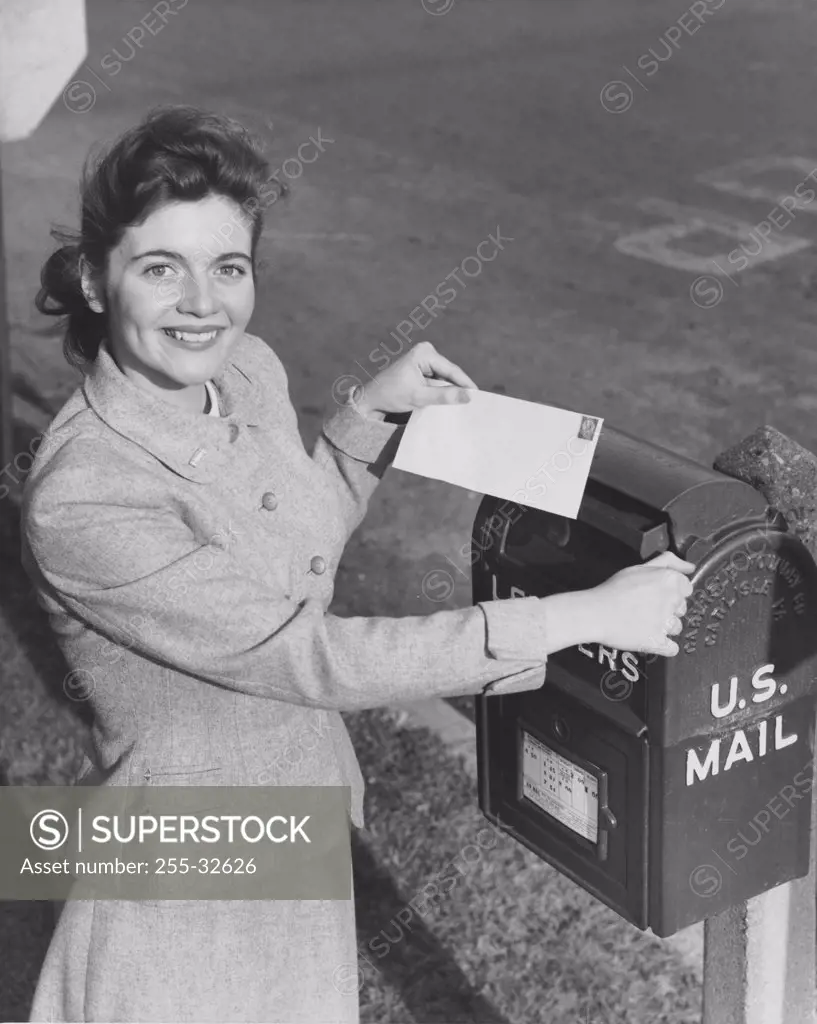 Young woman dropping a letter into a mailbox
