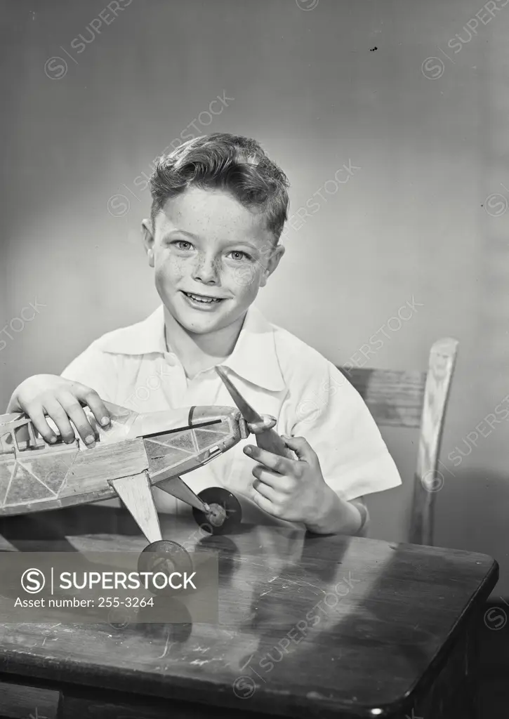 Vintage Photograph. Young smiling boy twirling propeller on toy airplane sitting on table