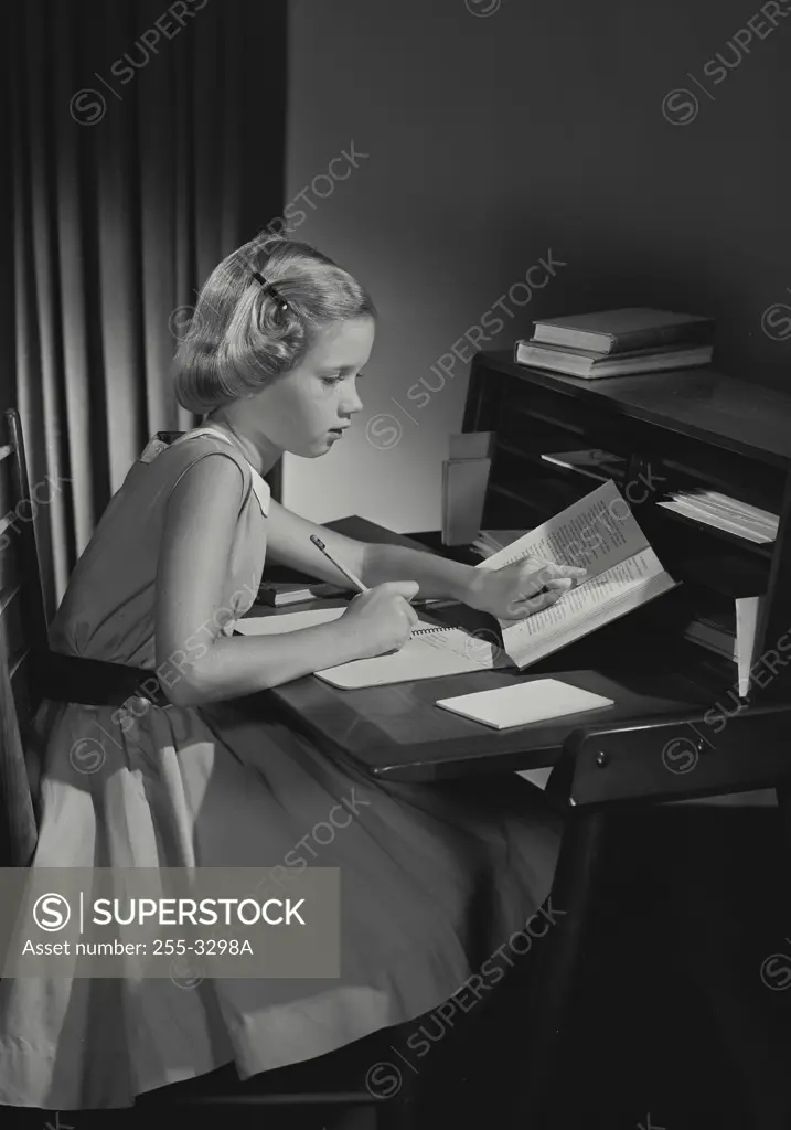 Vintage Photograph. Young girl wearing dress sitting at desk doing homework, Frame 1