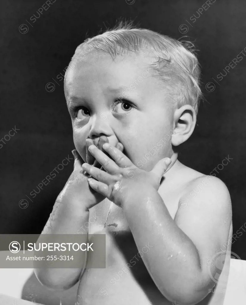 Close-up of a baby boy covering his mouth with his hands