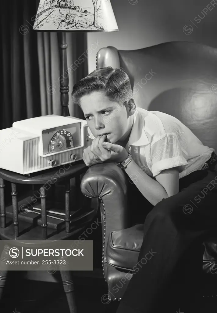 Vintage Photograph. Boy sitting by lamp and clock radio listening intensely biting nails