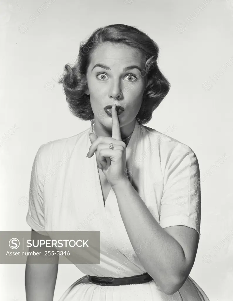 Vintage Photograph. Young woman wearing white dress with finger on lips making hush expression