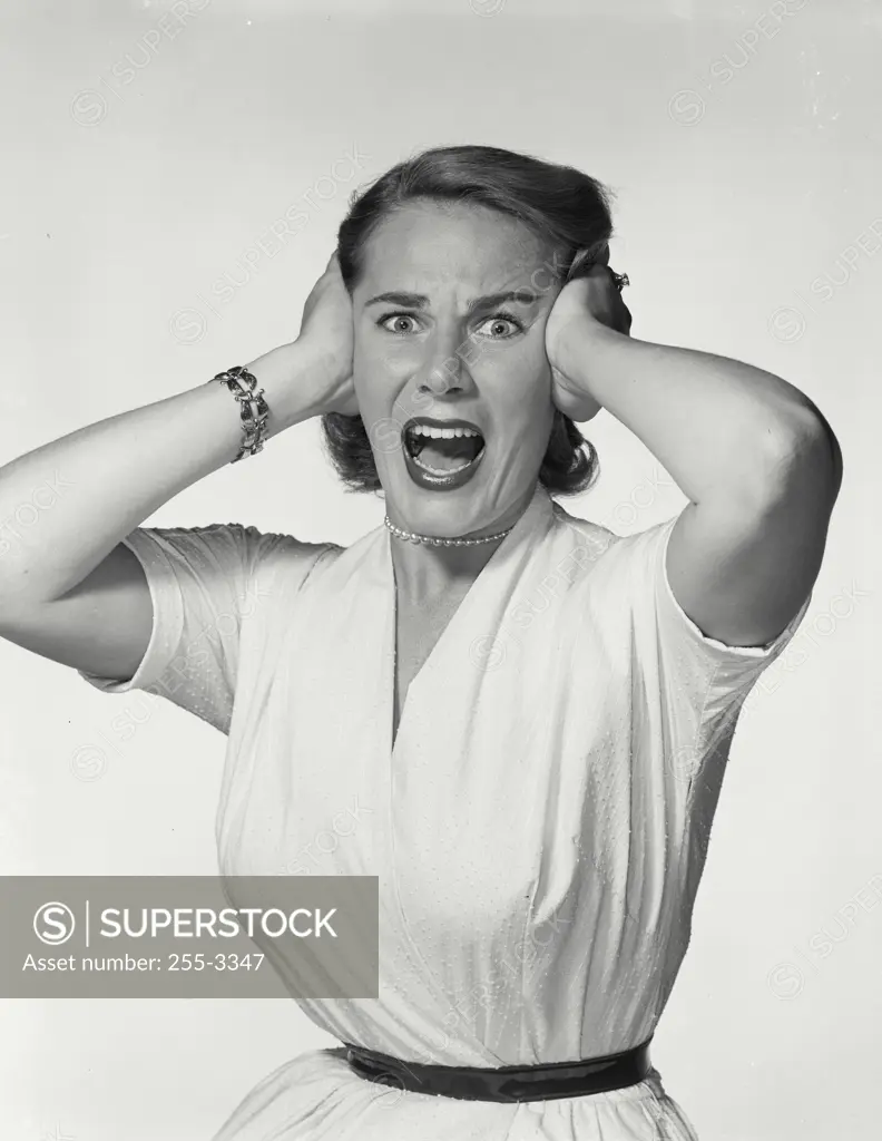 Vintage Photograph. Young woman wearing white dress pressing hands to head screaming in frustration