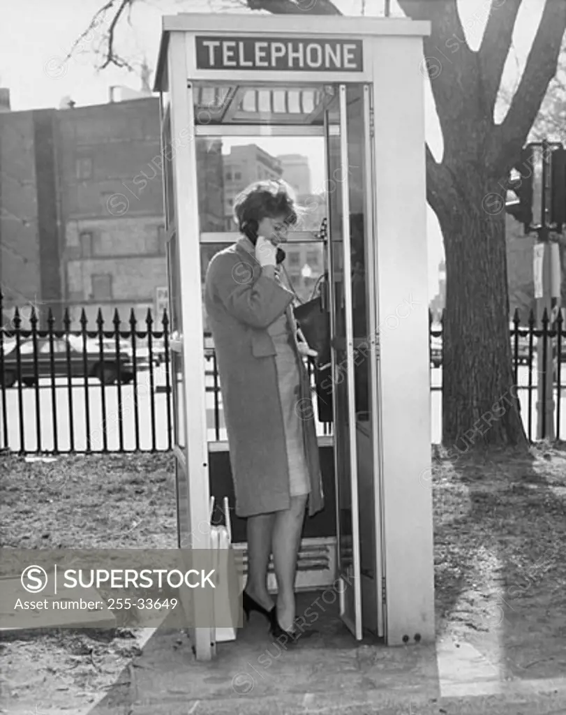 Side profile of a young woman talking on the phone in a telephone booth