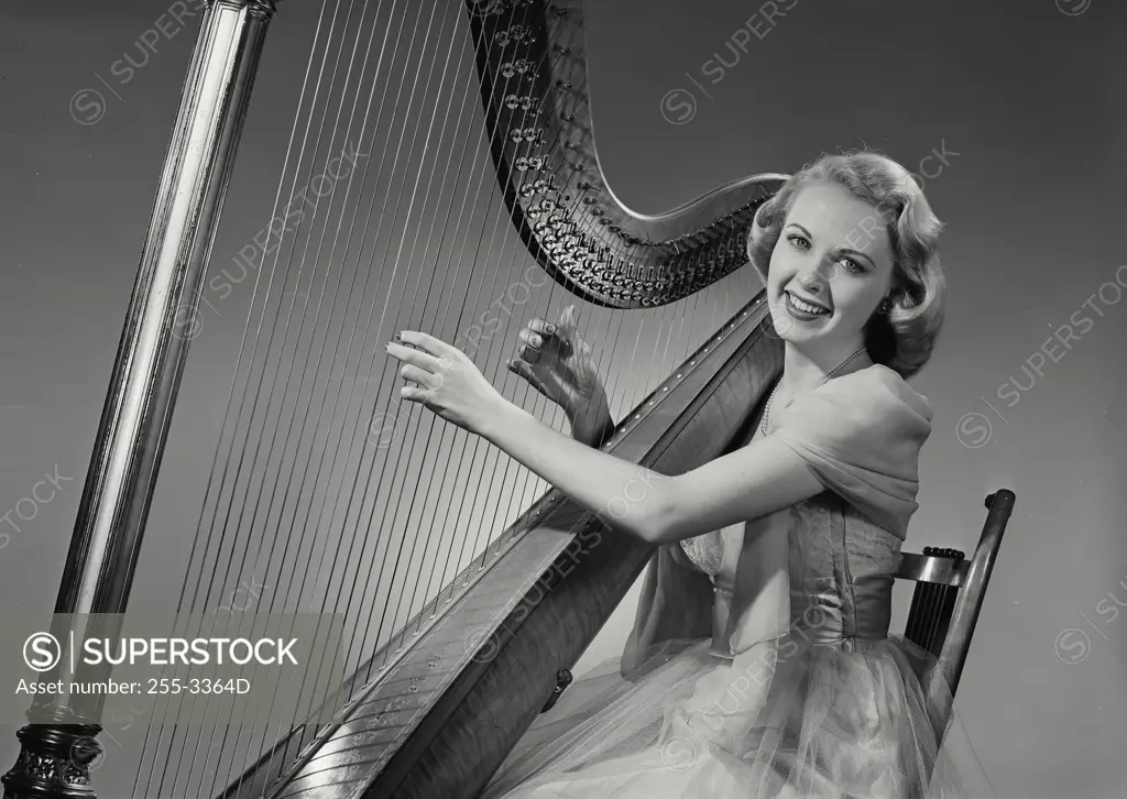 Vintage Photograph. Woman in dress smiling and playing Grand Pedal Harp. Frame 1