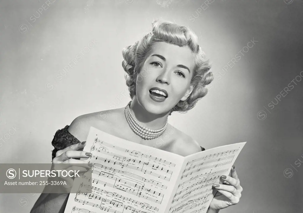 Vintage photograph. Portrait of woman in lace dress singing from sheet music