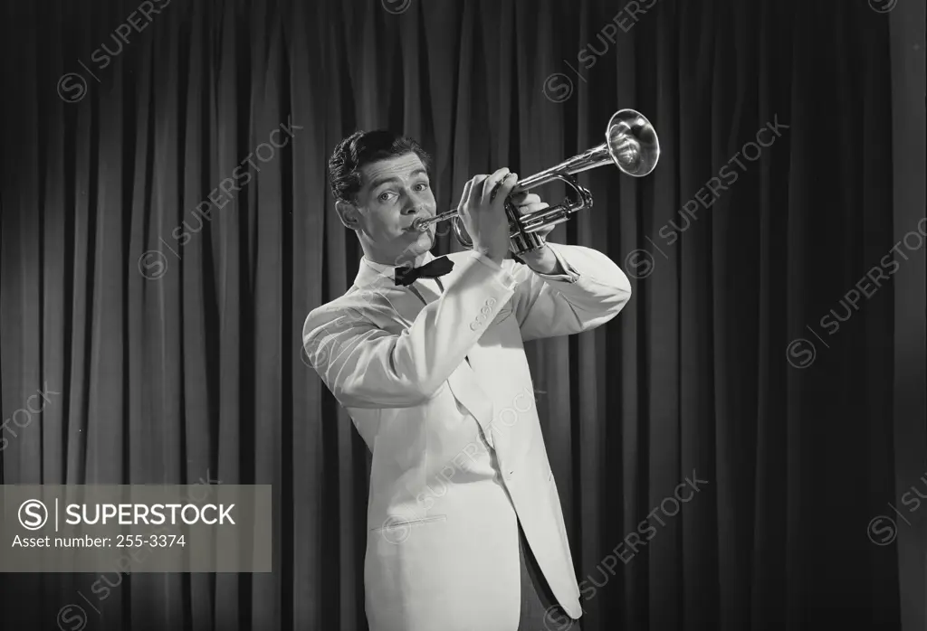 Vintage Photograph. Young man wearing white tuxedo playing trumpet standing in front of wall of curtains