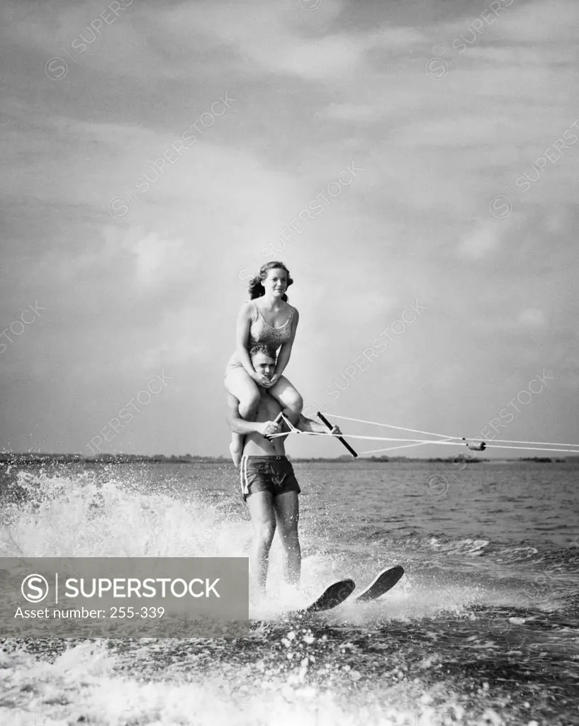 Young man waterskiing in sea with young woman sitting on his shoulders
