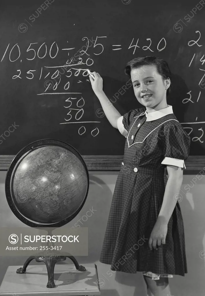 Vintage photograph. Young girl in dress writing on chalkboard