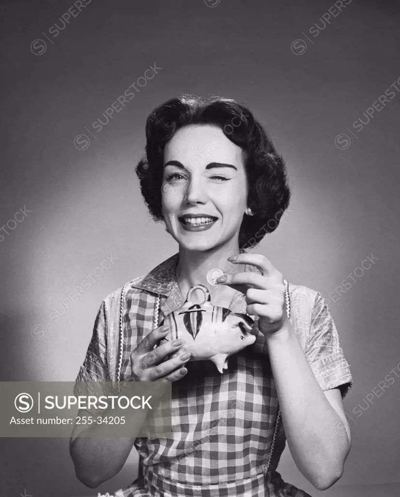 Close-up of a young woman holding a piggy bank and winking