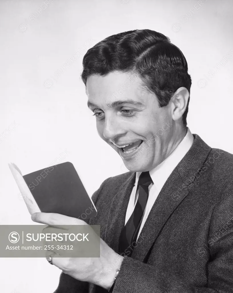 Close-up of a young man holding a bankbook and laughing