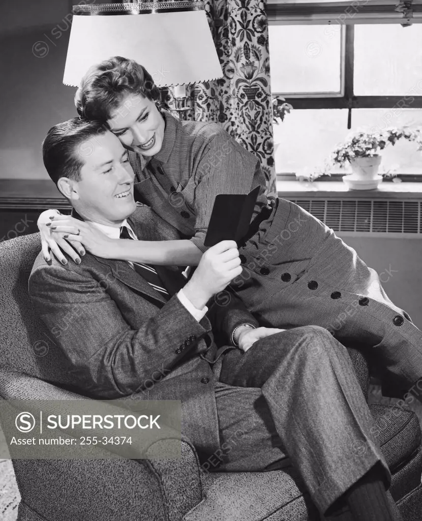 Mid adult man holding a bankbook with a mid adult woman embracing him