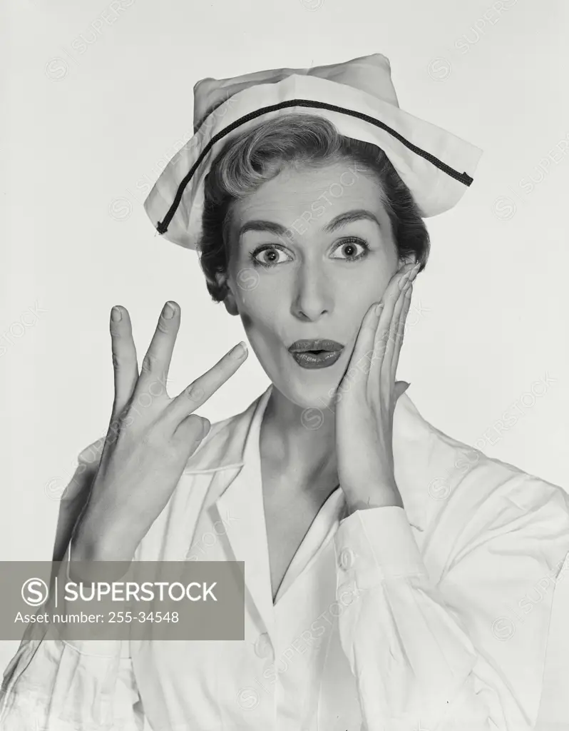 Vintage Photograph. Woman wearing nurse uniform holding up three fingers on right hand, other hand resting on cheek with surprised expression