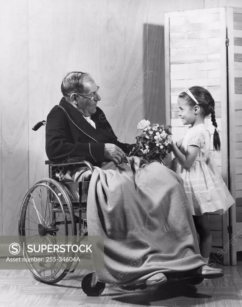Girl giving a bouquet of flowers to her grandfather sitting in a wheelchair