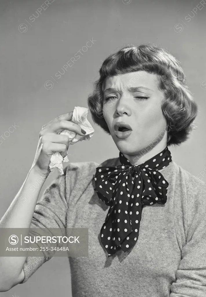 Vintage photograph. Woman with short bangs sneezing holding up tissue
